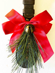 Rustic equestrian leather ornament door greeter with red bow and bronze jingle bell for holiday decor.