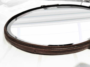 Oval leather mirror with waxed bridle frame and nickel snaffle bit hanging, measuring 12"x16".